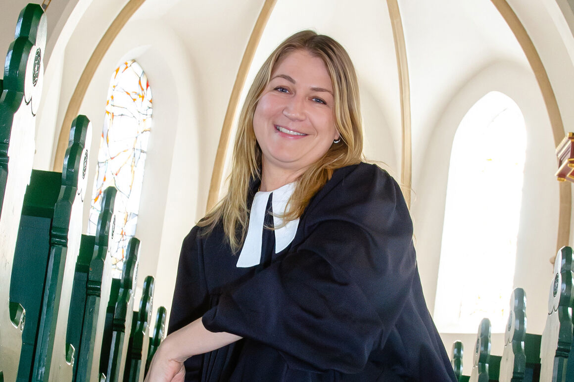 Eine als Frau lesbare Person hockt im Talar in einer Kirche